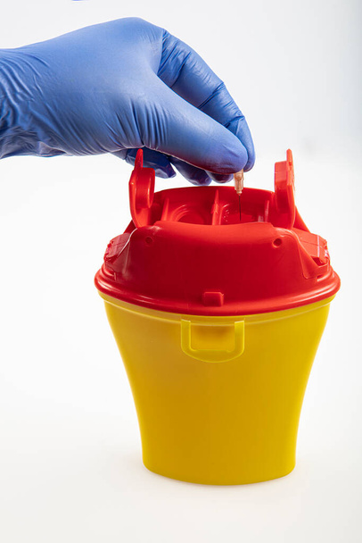 Health worker throws sharp waste into the medical waste bin. Medical waste bin pocket size 0,4 liter. Yellow biohazard medical contaminated clinical waste container isolated on white background. - Foto, afbeelding