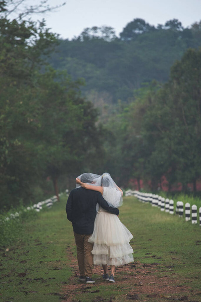 カップル、花嫁カバー新郎とともに彼女のベールを歩く光を注ぐ雨の中で - 写真・画像