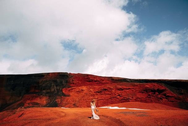 Portret modelki panny młodej w złotej sukni ślubnej, w żółto-czerwonym, piaszczystym kamieniołomie, w kraterze wulkanu na Islandii, Golden Circle. Bukiet zaczepów i złotych gałęzi. - Zdjęcie, obraz
