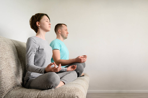 Father and daughter are meditating, sitting in lotus position on the couch. Yoga at home. - Foto, imagen
