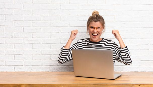 young pretty latin woman feeling happy, surprised and proud, shouting and celebrating success with a big smile sitting with her laptop - Фото, изображение