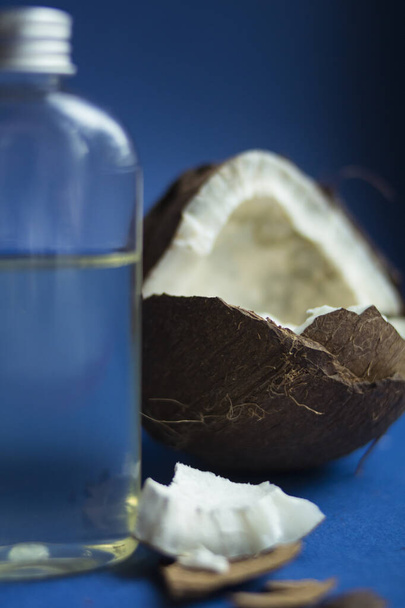 Bella noce di cocco aperta con olio di cocco fuso trasparente liquido su sfondo blu
 - Foto, immagini