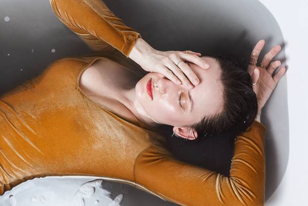 Sobre el retrato de una joven mujer adulta acostada en una bañera llena de agua de carbón
 - Foto, Imagen