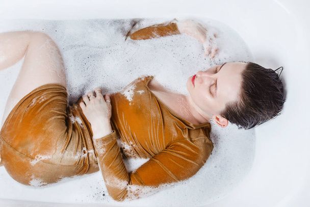 Above portrait of young adult woman lying in bathtub filled with charcoal bath bomb - Foto, Imagen