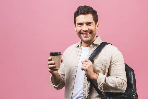 Young handsome man with backpack holding coffee cup isolated on pink background. Smiling student portrait. Studio shot of cheerful men going on travel. - Φωτογραφία, εικόνα