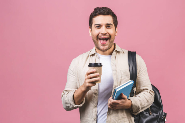 Fiatal, jóképű férfi hátizsákkal, aki rózsaszín háttéren tartja a kávéspoharat. Mosolygó diákportré. Stúdió felvétel vidám emberek mennek az utazás. - Fotó, kép
