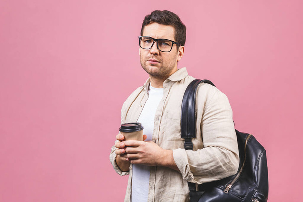 Fiatal, jóképű férfi hátizsákkal, aki rózsaszín háttéren tartja a kávéspoharat. Komoly diákportré. Stúdió felvétel vidám emberek mennek az utazás. - Fotó, kép