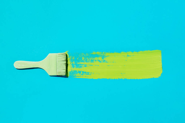 Flatlay of colored brush with swoosh of green paint on blue - Foto, Bild