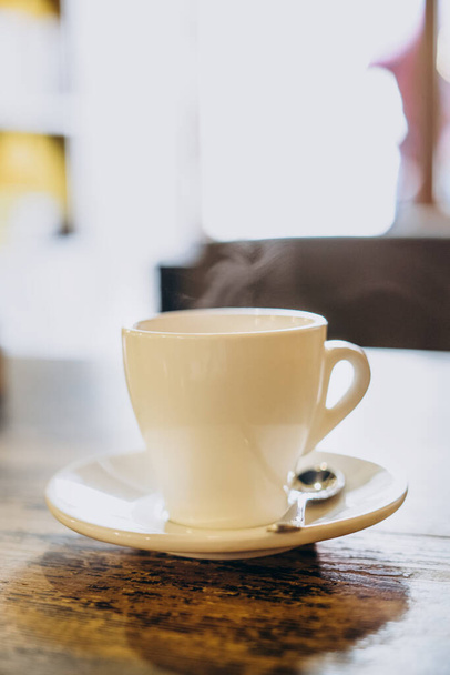 Fehér csésze csészealjjal és kis kanállal egy fa asztalon. Forró eszpresszó fehér pohárban. Finom kávé reggelire egy kávézóban. - Fotó, kép