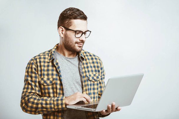 Selbstbewusster Wirtschaftsexperte. Selbstbewusster junger gutaussehender Mann im Hemd, Laptop in der Hand und lächelnd vor weißem Hintergrund  - Foto, Bild