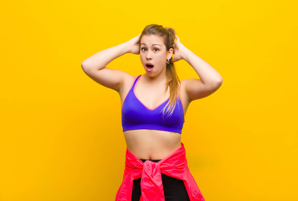 young blonde woman looking excited and surprised, open-mouthed with both hands on head, feeling like a lucky winner. sport concept - Foto, imagen