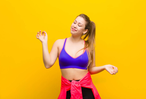 young blonde woman smiling, feeling carefree, relaxed and happy, dancing and listening to music, having fun at a party. sport concept - Foto, imagen