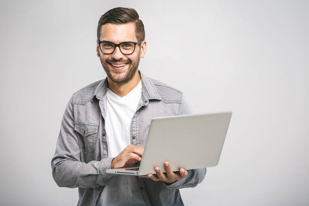 Confident business expert. Confident young handsome man in shirt holding laptop, looking at camera and smiling while standing against white background - Fotó, kép