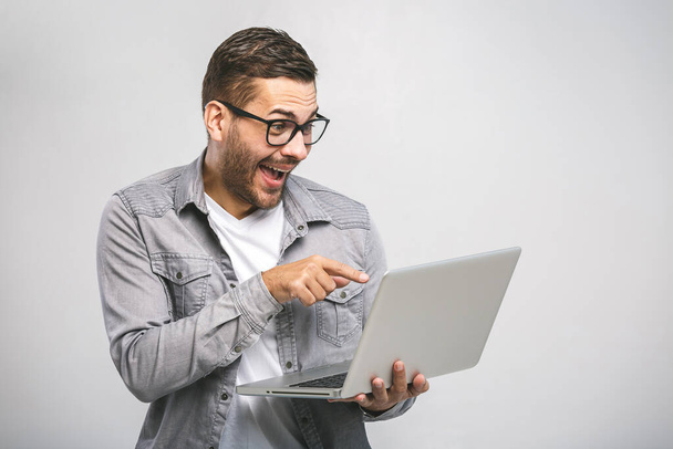 Pewny siebie młody przystojny mężczyzna w koszuli trzyma laptopa i uśmiecha się stojąc na białym tle - Zdjęcie, obraz