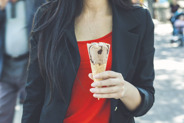 donna d'affari cammina all'aperto e mangia gelato alla vaniglia in una giornata estiva soleggiata. Primo piano delle mani femminili con cono gelato
 - Foto, immagini