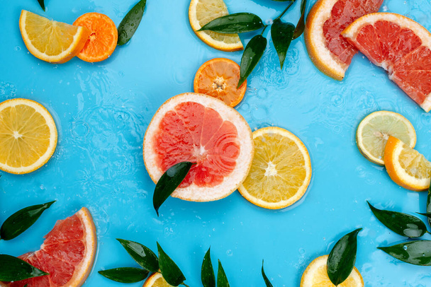 Flatlay of various citrus fruits and leaves on blue background with drops of water - Photo, Image