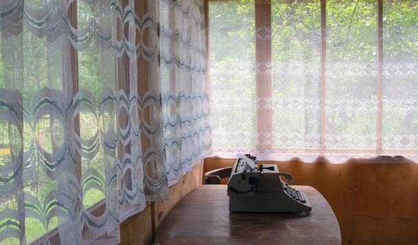 Maison de vacances. Intérieur rétro avec murs en bois, rideaux en tulle sur les fenêtres. Une machine à écrire se tient sur une vieille table en bois
 - Photo, image