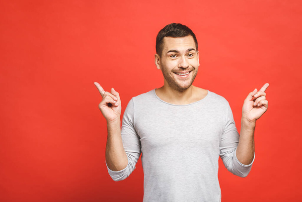 Šťastný usmívající se mladý muž představuje a ukazuje váš text nebo produkt izolované na červeném pozadí. - Fotografie, Obrázek
