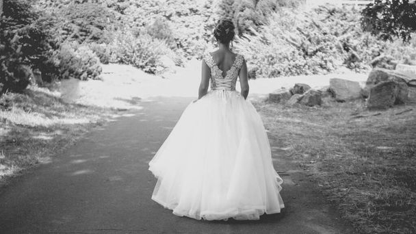 Foto in bianco e nero di elegante giovane sposa in abito lungo passeggiando al parco
 - Foto, immagini
