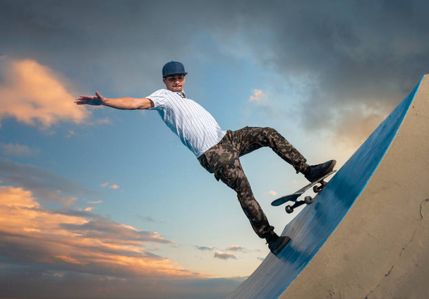 mladý skateboardista spadne ze svého skateboardu při jízdě podél okraje rampy ve večerním světle - Fotografie, Obrázek