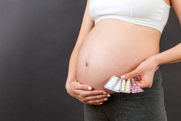 Przycięty obraz ciężarnej kobiety trzymającej tabletki na kolorowym tle z przestrzenią do kopiowania. Problemy zdrowotne podczas ciąży. - Zdjęcie, obraz