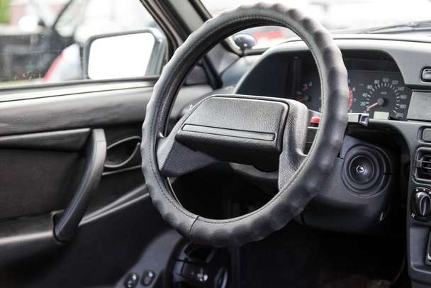 Egy orosz régi autó kormánykerekének közelsége egy fekete műanyag vezérlőpulton, gyújtáskapcsolóval és az utastérben a motor fordulatszámára és hőmérsékletére vonatkozó érzékelőkkel. - Fotó, kép