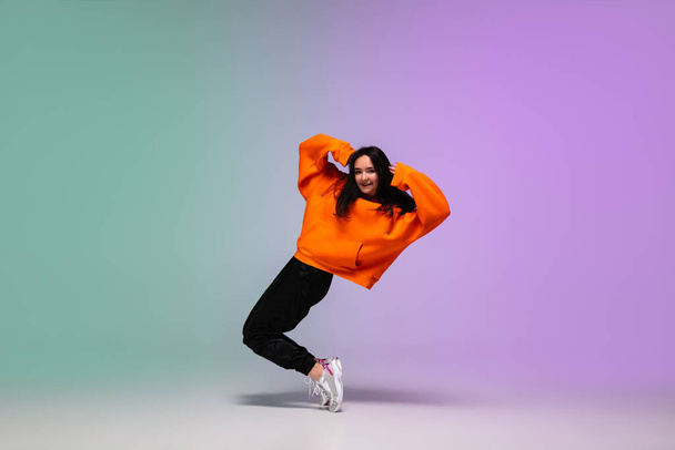 Girl dancing hip-hop in stylish clothes on gradient background at dance hall in neon light. - Foto, Imagem