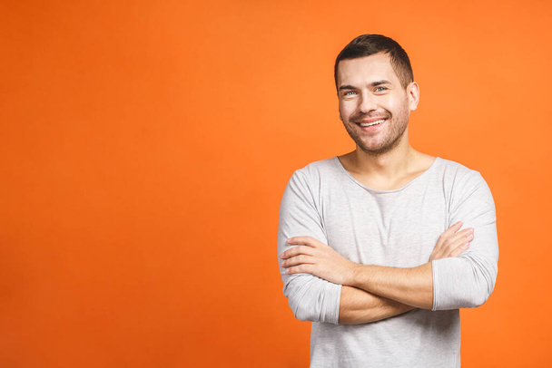 Casually handsome. Confident young handsome man keeping arms crossed and smiling while standing against orange background. - Photo, Image