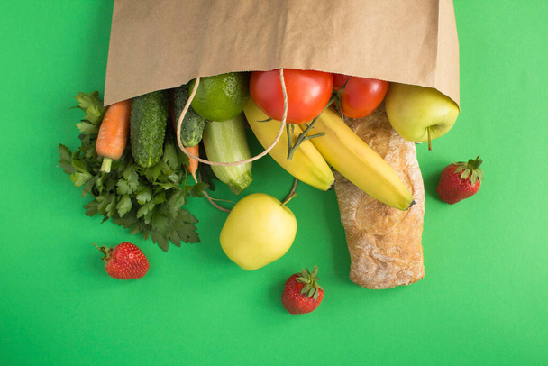 Papírzacskó zöldségekkel, gyümölcsökkel és bagettel a zöld háttéren. Zsákos kaja koncepció. Felülnézet.Másolja a helyet. - Fotó, kép