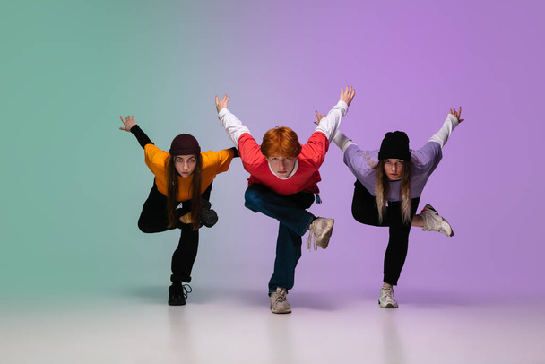 Group of teens, boys and girls dancing hip-hop in stylish clothes on gradient studio background in neon light. - Foto, Imagem