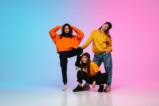 Girls dancing hip-hop in stylish clothes on gradient background at dance hall in neon light. - 写真・画像