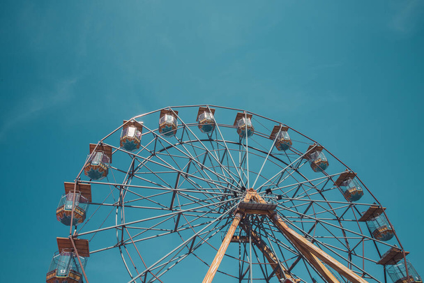 A distant view of a the top half of a symmetrical, vintage Ferris Wheel at a seaside fairground with copy space and blue sky background - Photo, image