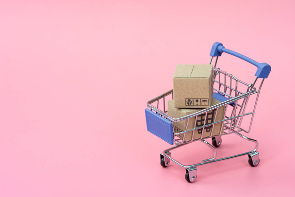 Concepto de compra: Cartones o cajas de papel en azul carrito de compras sobre fondo rosa. los consumidores de compras en línea pueden comprar desde el hogar y el servicio de entrega. con spac de copia - Foto, imagen