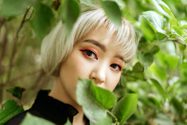 Young blonde asian female in green leaves, shallow selective focus - Фото, зображення