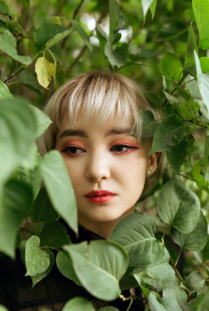Young blonde asian female in green leaves, shallow selective focus - 写真・画像