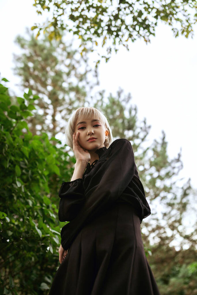 Young adult blonde asian female in dark clothes looking down, selecitve focus - Foto, imagen