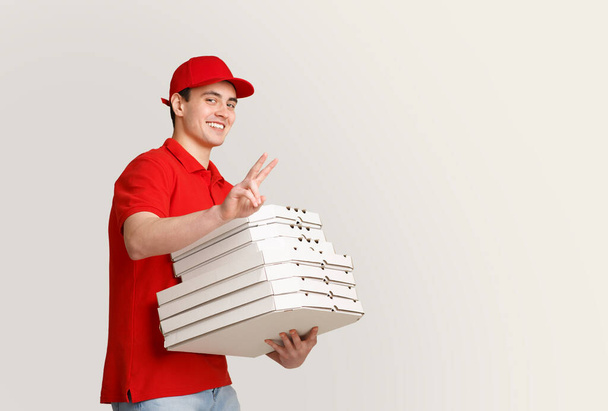 Hodně pizzy až domů. Usmívající se kurýr ukazuje mírové znamení a drží mnoho krabic - Fotografie, Obrázek