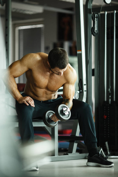 Γυμναστική, άθληση και υγιεινό τρόπο ζωής έννοια. Όμορφος αθλητικός άντρας με γυμνό κορμό να κάνει ασκήσεις. Bodybuilder αρσενικό μοντέλο κατάρτισης δικέφαλους μυς με αλτήρα - Φωτογραφία, εικόνα