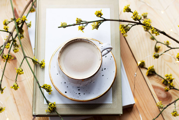 Una taza de café y un libro sobre un fondo de madera con flores amarillas. Lugar de trabajo. Acogedor desayuno. Concepto primavera
 - Foto, Imagen