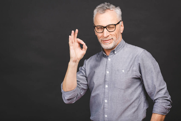 Portrait of businesslike senior aged man 50s with grey hair and beard in shirt smiling and gesturing ok sign isolated against black background. - Photo, Image
