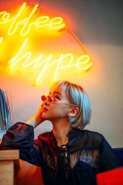 Young adult asian female wearing sunglasses in front of neon light  - Foto, afbeelding