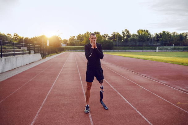 Homme handicapé caucasien beau et sportif avec jambe artificielle debout sur l'hippodrome et se préparant à courir
. - Photo, image