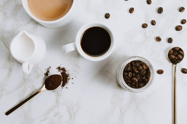 Flatlay of fresh cups of espresso and milk coffee, creamer, coffee beans and spoon on marble background, selective focus - Photo, image
