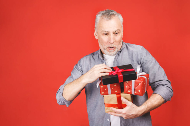 Omg! Portrait, happy super excited senior man, opened, unwrapped gift boxes, isolated against red background, enjoying his present. Positive human emotion, facial expression, feeling attitude, reaction. - Photo, Image