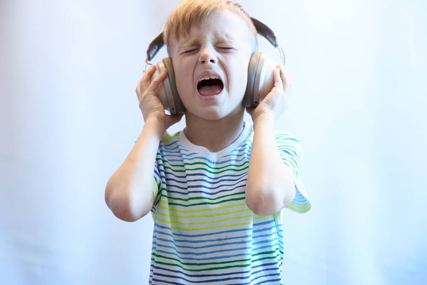 Забавный мальчик в наушниках слушает музыку и поет песню - Фото, изображение