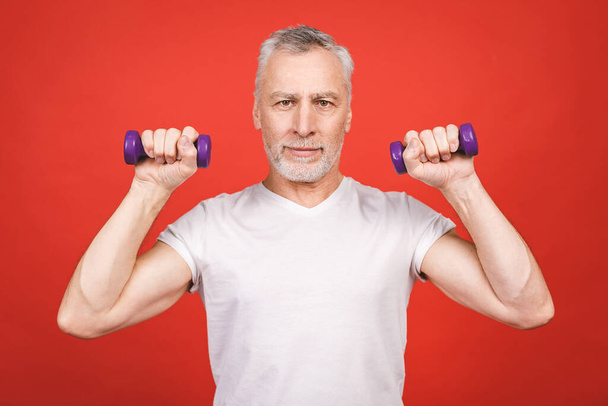 Portrét staršího muže Cvičení s činkami na červeném pozadí. - Fotografie, Obrázek