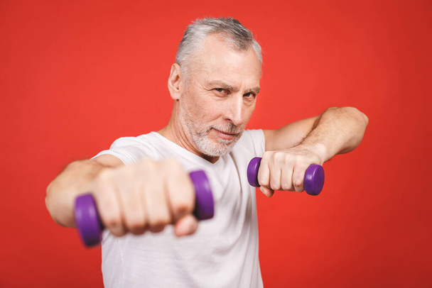 Close-up portrait Of A Senior Man Exercising with dumbbells against red Background. - Valokuva, kuva