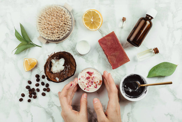Flatlay of woman's hands holding homemade rose buds cream with the ingredients and other natural home beauty products on the side - Valokuva, kuva