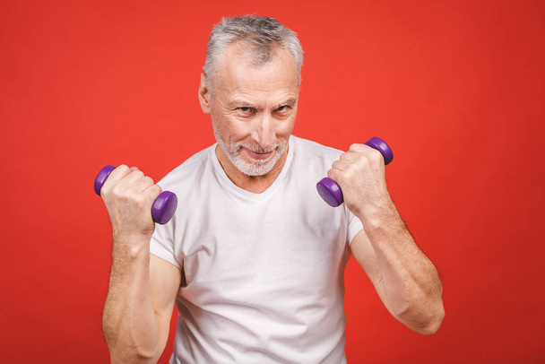 Close-up retrato de um homem sênior se exercitando com halteres contra fundo vermelho
. - Foto, Imagem