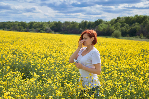 Allergic to pollen and flowering season, a girl sneezes in a flower field - Photo, Image